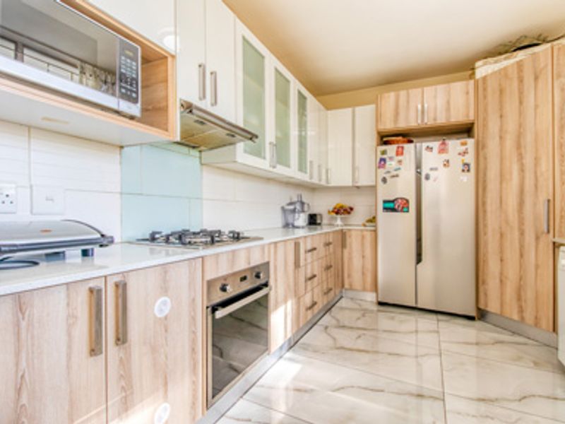Modern kitchen featuring light wood-grain cabinetry, white stone countertops, built-in oven, gas hob, extractor fan, and integrated microwave with polished marble-look floor tiles.