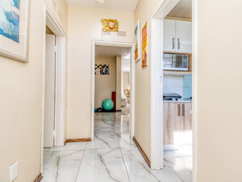 A bright hallway featuring modern marble-look floor tiles, providing access to the kitchen and adjacent living areas within the apartment.