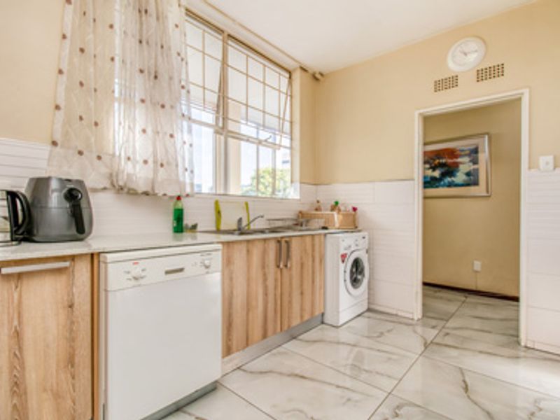 Functional kitchen featuring wood-look cabinetry, tiled flooring, stainless steel sink, and dedicated space for a dishwasher and washing machine.