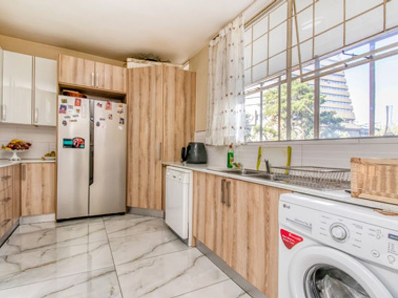 A functional kitchen featuring light wood-grain cabinetry, marble-look floor tiles, a double sink, and integrated space for laundry appliances.
