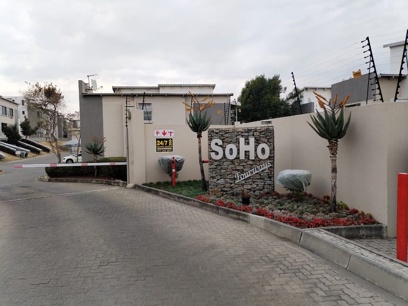 The entrance to SoHo Fourways apartment complex featuring a secure boom gate, stone signage wall, and well-maintained perimeter electric fencing.