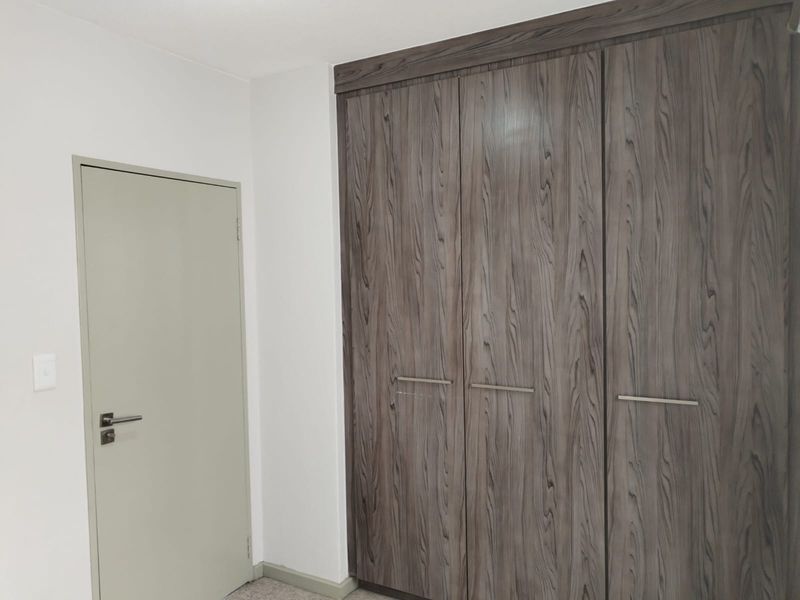 A clean bedroom interior featuring modern wood-grain built-in cupboards and a neutral-toned internal door.