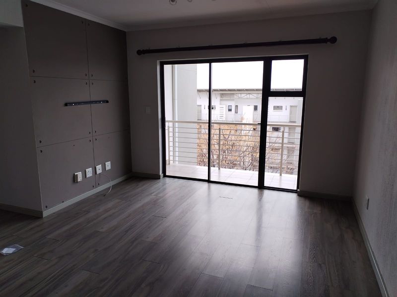 An empty living room featuring modern laminate flooring, a decorative feature wall, and large sliding glass doors providing access to a private balcony.