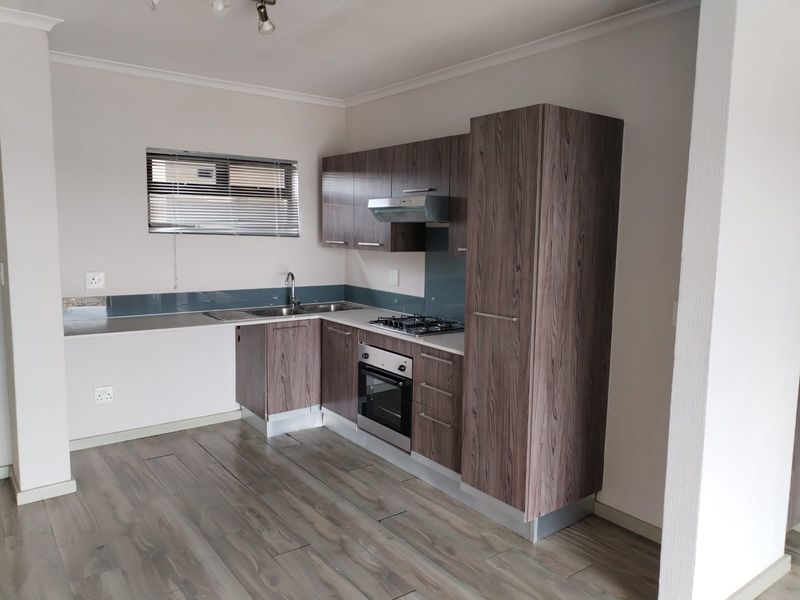 A modern, clean kitchen featuring wood-look laminate cabinetry, built-in oven, gas hob, extractor fan, and a sleek glass splashback.