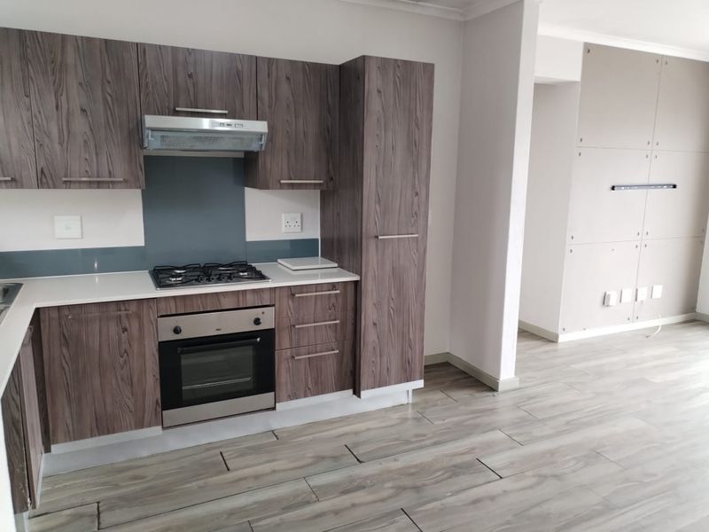 Modern kitchen featuring wood-grain cabinetry, stone countertops, gas hob, electric oven, and integrated extractor fan, finished with durable laminate flooring.