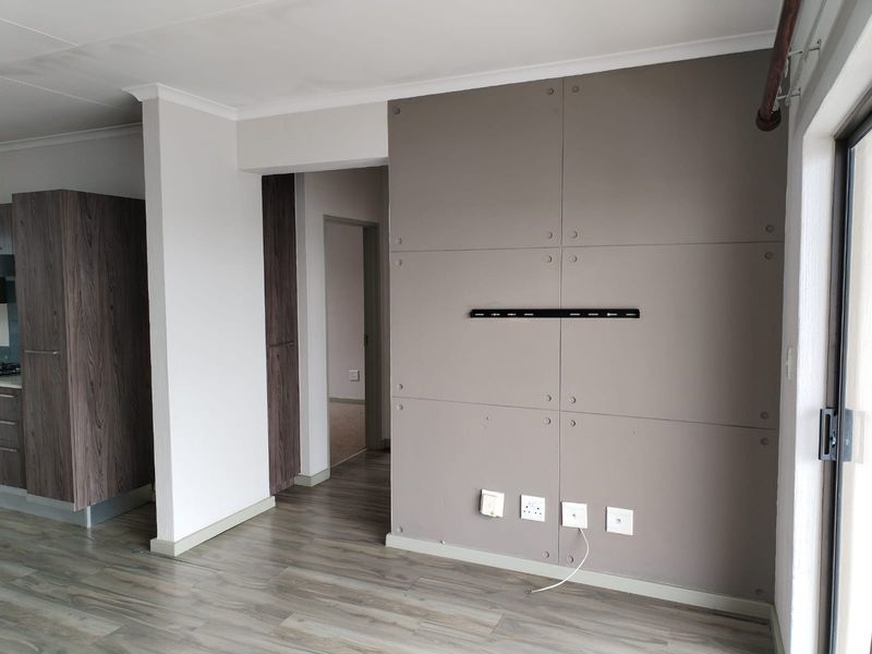 A bright, empty living area featuring modern laminate flooring, a decorative feature wall with integrated TV mount, and access to an outdoor space.