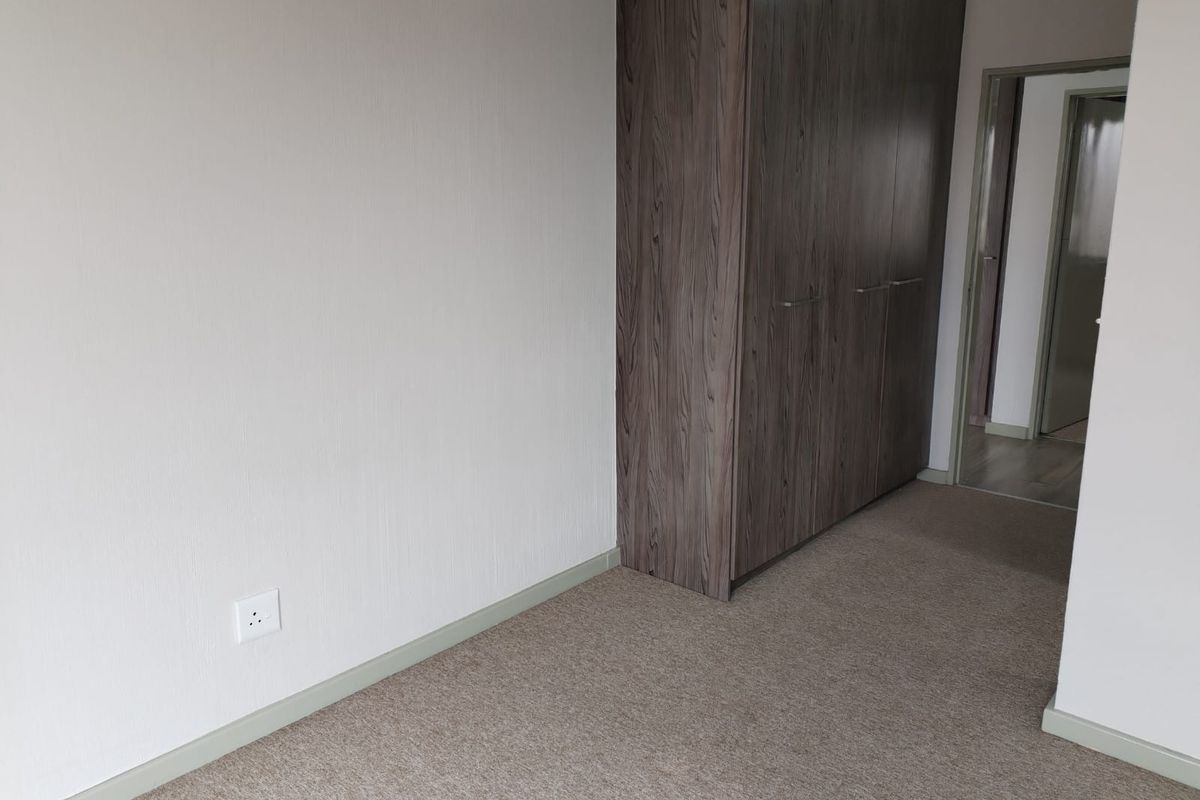 A clean, empty bedroom featuring neutral carpeting and modern wood-finish built-in cupboards, offering a versatile space ready for personalization.