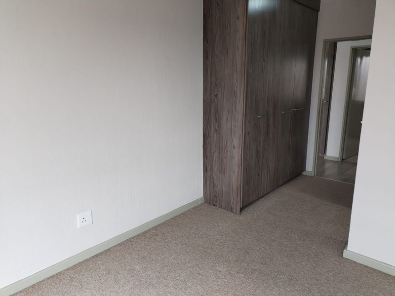A clean, empty bedroom featuring neutral carpeting and modern wood-finish built-in cupboards, offering a versatile space ready for personalization.