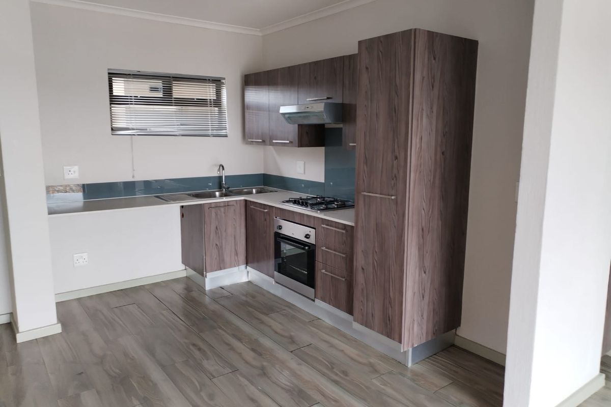 Modern kitchen featuring wood-look laminate cabinetry, built-in oven, gas hob, extractor fan, and a sleek glass splashback with durable laminate flooring.