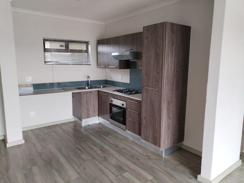 Modern kitchen featuring wood-look laminate cabinetry, built-in oven, gas hob, extractor fan, and a sleek glass splashback with durable laminate flooring.