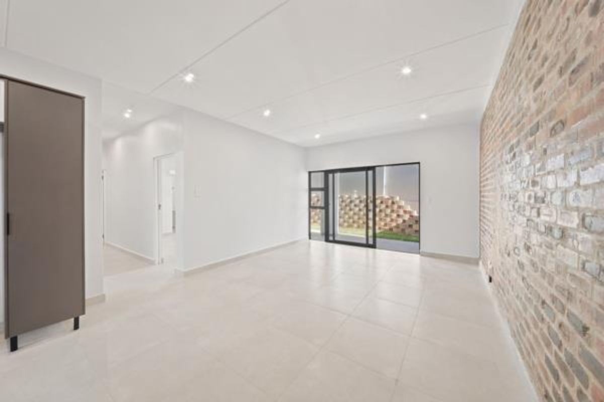 A bright, modern living area featuring a striking exposed brick feature wall, neutral tiled flooring, and large sliding glass doors leading to the exterior.