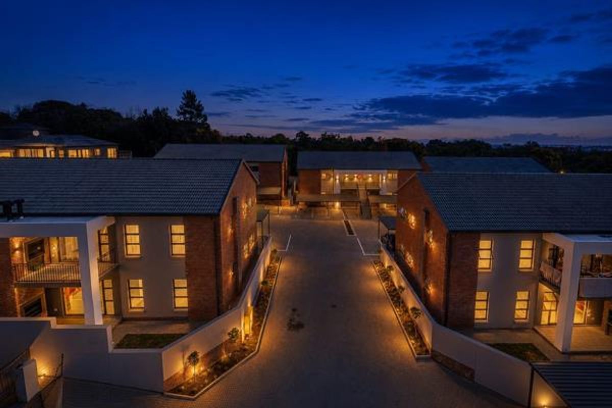 Aerial evening view of a modern apartment complex featuring brick and rendered facades, tiled roofs, and illuminated paved driveways.