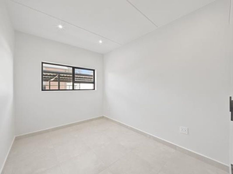A bright, modern, and empty bedroom featuring neutral tiled flooring, recessed downlights, and built-in cupboards, offering a clean canvas for personalization.
