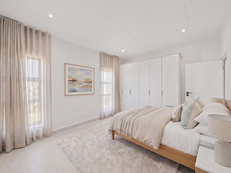 A bright and modern bedroom featuring neutral tones, tiled flooring, recessed downlights, and ample built-in cupboard storage.
