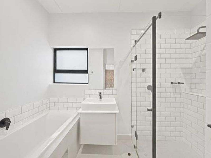 Modern bathroom featuring a built-in bathtub, wall-mounted vanity, and a glass-enclosed shower with subway tiling and contemporary black matte fixtures.