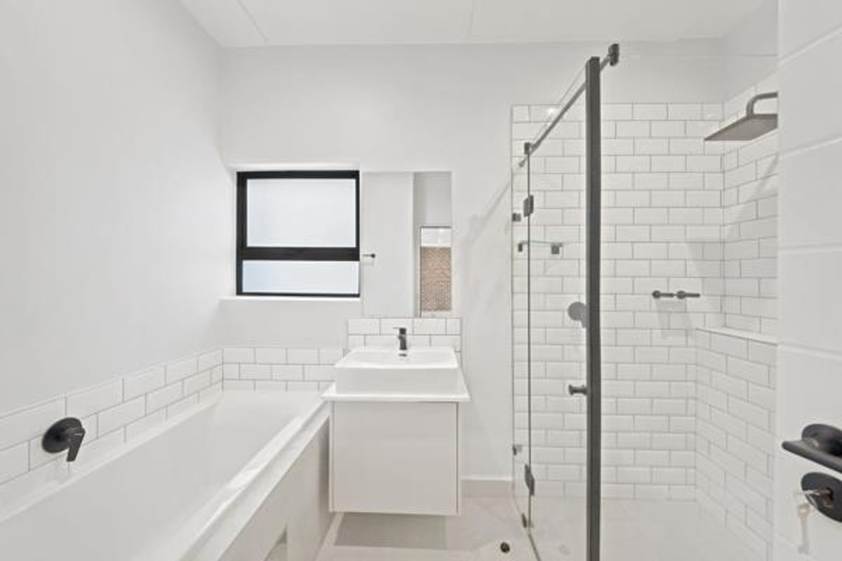 Modern bathroom featuring a built-in bathtub, wall-mounted vanity, and a glass-enclosed shower with subway tiling and contemporary black matte fixtures.