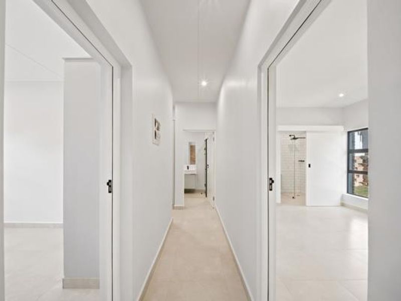 A bright, modern hallway with neutral tiled flooring and recessed lighting, providing access to adjacent rooms including a bathroom with a walk-in shower.