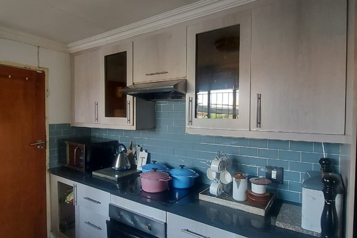 A functional kitchen featuring light-toned cabinetry, a dark countertop, and a blue subway tile backsplash with an integrated extractor fan.