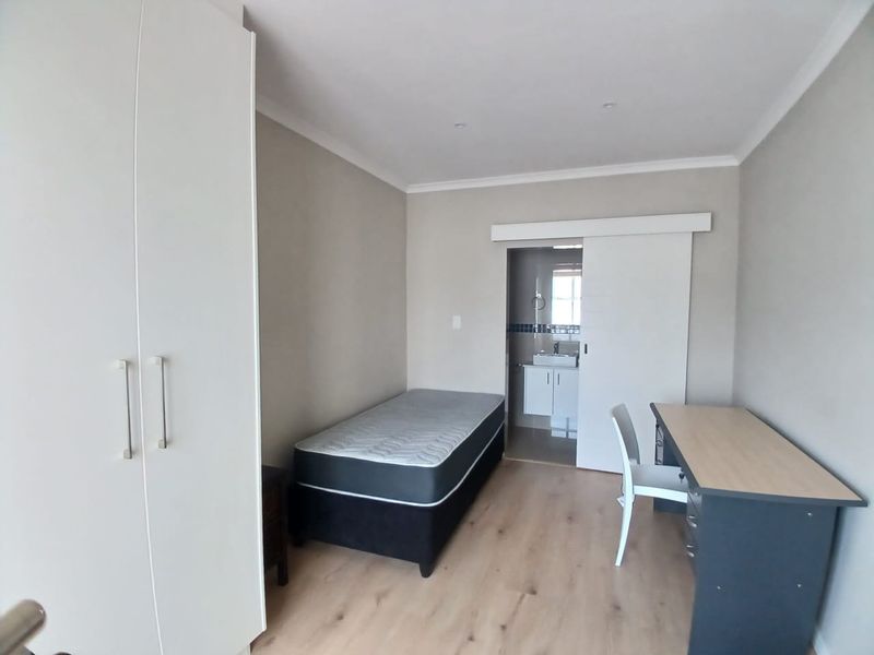 A modern bedroom featuring laminate flooring, built-in wardrobes, and an en-suite bathroom accessed via a sliding door.