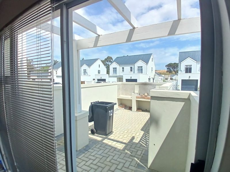 A paved outdoor patio area featuring a built-in braai and a pergola structure, viewed from an interior sliding door.