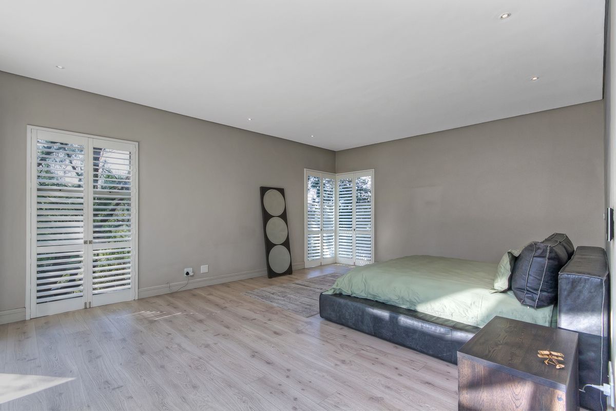 Spacious bedroom featuring light wood-look flooring, neutral wall tones, and white plantation shutters on the windows.