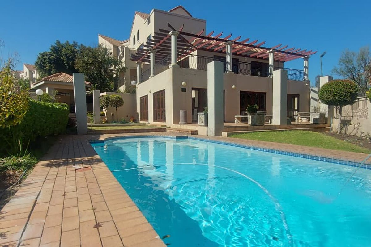 A well-maintained outdoor pool area featuring a swimming pool, brick paving, and a covered pergola attached to the townhouse structure.