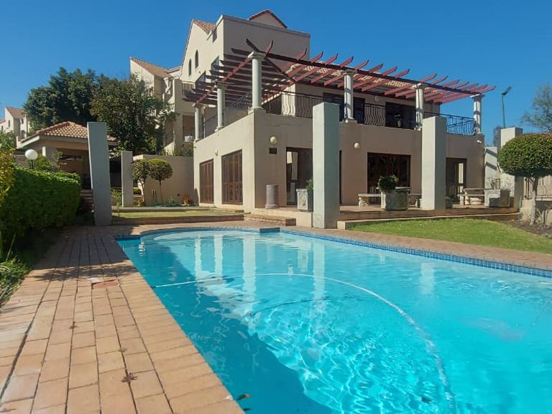A well-maintained outdoor pool area featuring a swimming pool, brick paving, and a covered pergola attached to the townhouse structure.