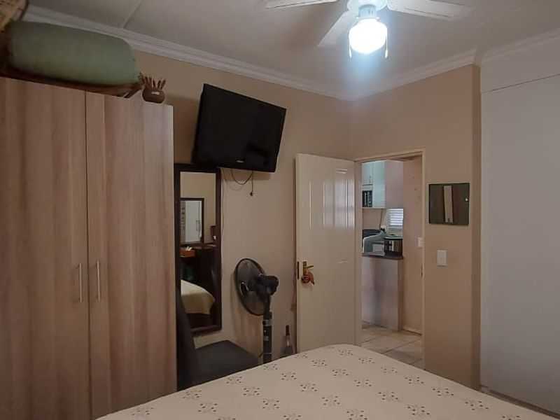A functional bedroom featuring built-in cupboards, a ceiling fan, and coving, with direct access to an adjacent room.