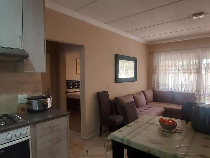 Open-plan living area featuring a functional kitchen with gas hob and oven, flowing into a lounge space with access to a patio through sliding doors.