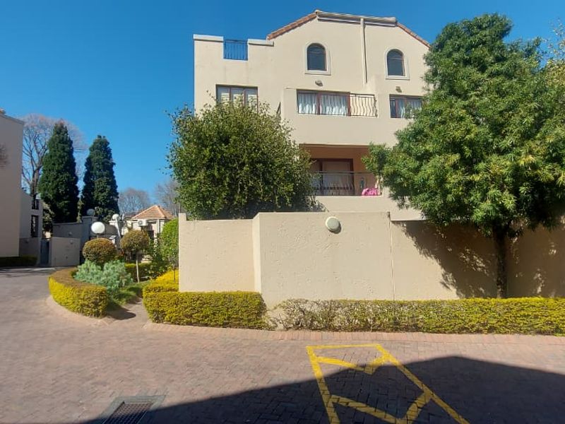 Front exterior view of a multi-story townhouse complex featuring paved driveway access, perimeter walling, and balcony access.