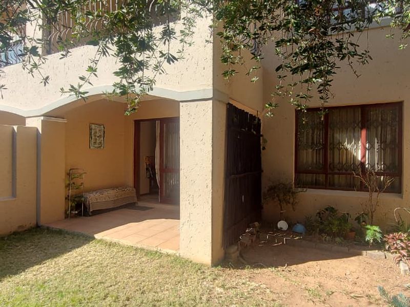 Rear view of the townhouse featuring a covered patio, tiled flooring, and a small private garden area with boundary walls.