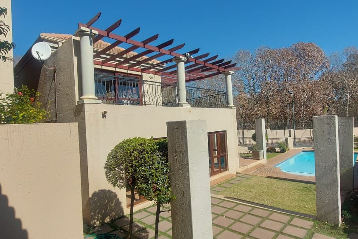 Rear view of the townhouse featuring a covered balcony with a pergola, a paved patio area, and a private swimming pool.