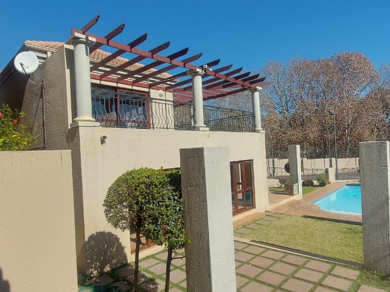 Rear view of the townhouse featuring a covered balcony with a pergola, a paved patio area, and a private swimming pool.