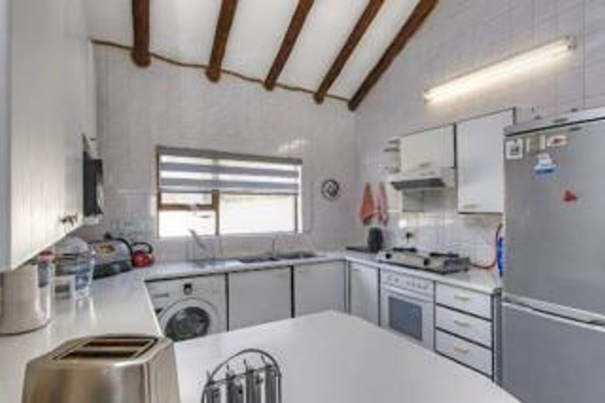 A functional kitchen featuring white cabinetry, a built-in oven with hob, extractor fan, and exposed timber ceiling beams.