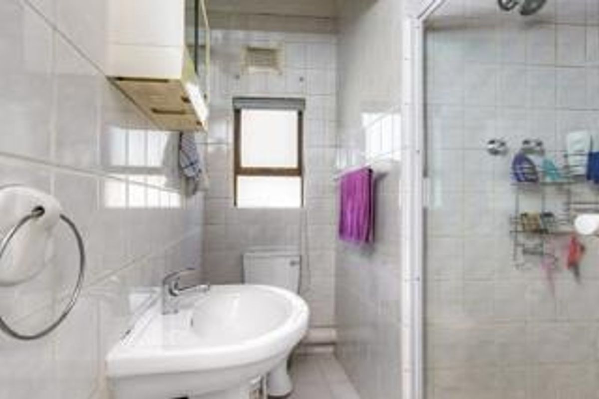 A functional bathroom featuring a pedestal sink, a glass-enclosed shower, and full-height wall tiling.
