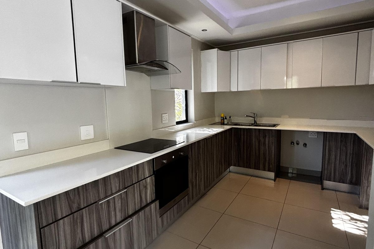 Modern kitchen featuring sleek two-tone cabinetry, white stone countertops, integrated oven, hob, extractor fan, and tiled flooring with recessed ceiling lighting.