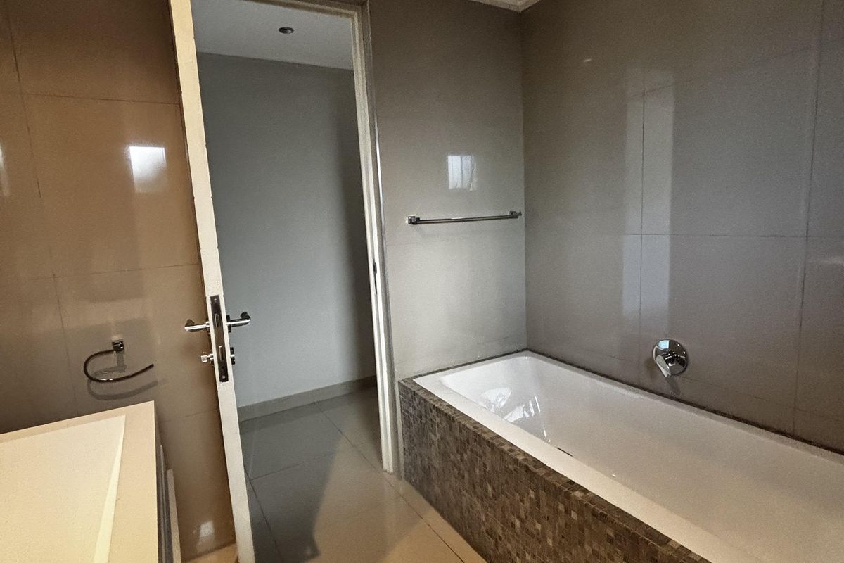 A modern bathroom featuring a built-in bathtub with mosaic tile detailing, large format wall tiles, and a vanity area.