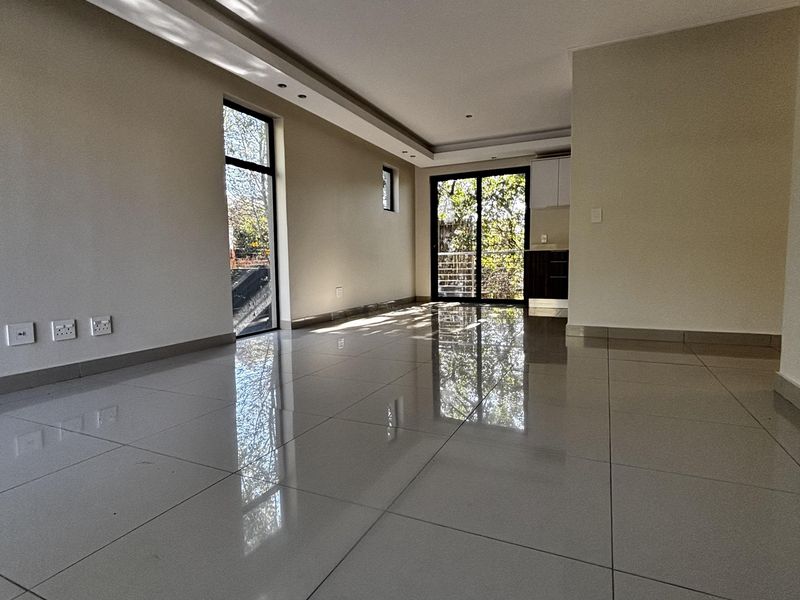 A bright, open-plan living area featuring polished porcelain floor tiles, recessed ceiling lighting, and large glass sliding doors leading to an outdoor space.