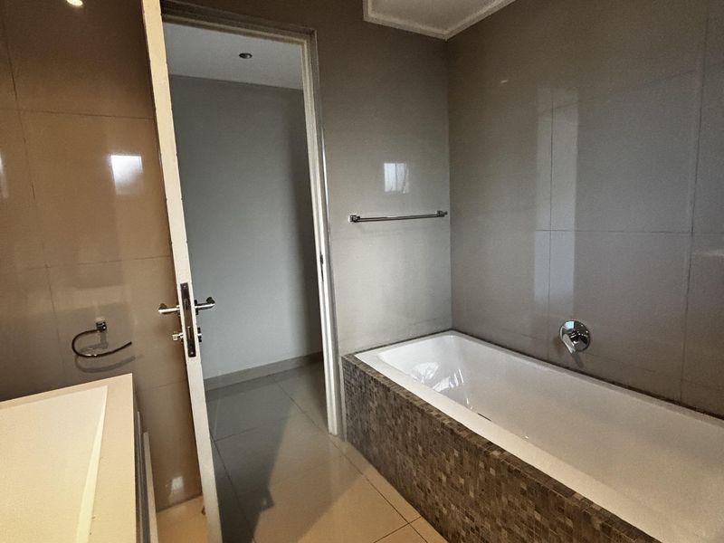 A modern bathroom featuring a built-in bathtub with mosaic tile detailing, large format wall tiles, and a vanity area.