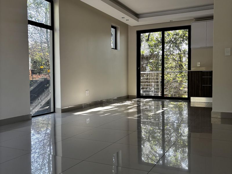 A bright, open-plan living area featuring polished porcelain floor tiles, recessed ceiling lighting, and large sliding glass doors leading to an outdoor space.
