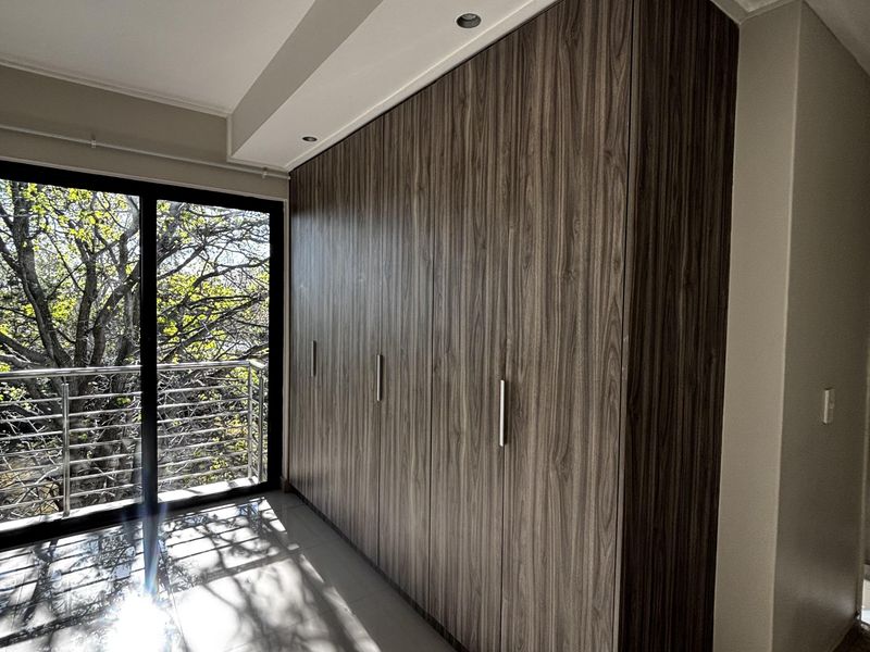 Bedroom featuring floor-to-ceiling built-in wooden cabinetry, tiled flooring, and a sliding glass door leading to a balcony with tree views.