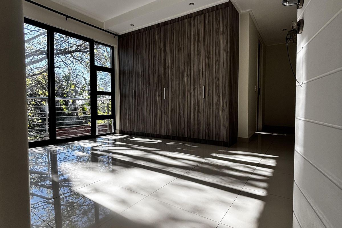 A bright bedroom featuring large glass sliding doors, polished floor tiles, and extensive built-in wooden cabinetry.