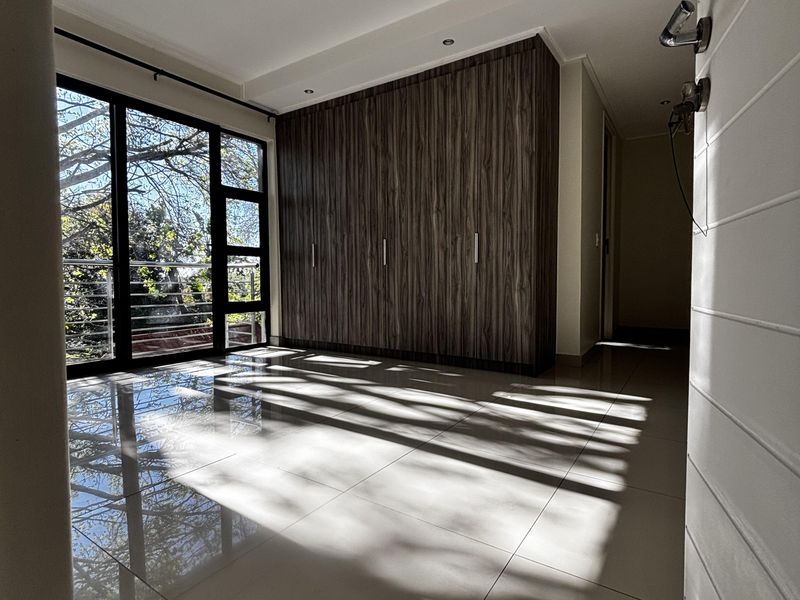A bright bedroom featuring large glass sliding doors, polished floor tiles, and extensive built-in wooden cabinetry.