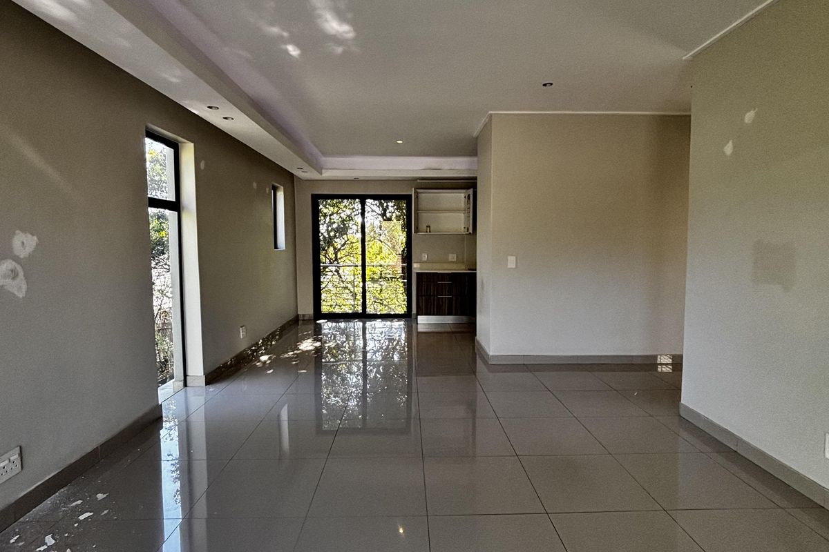 An open-plan living area featuring large format floor tiles, recessed ceiling lighting, and sliding glass doors leading to an outdoor space.