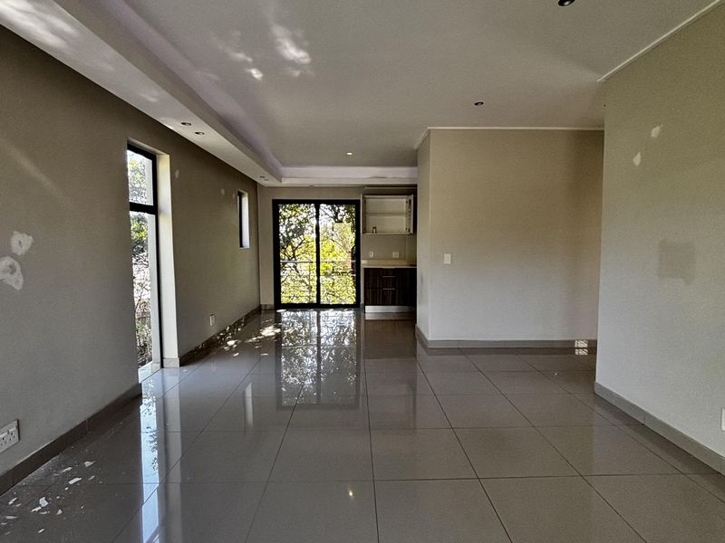 An open-plan living area featuring large format floor tiles, recessed ceiling lighting, and sliding glass doors leading to an outdoor space.