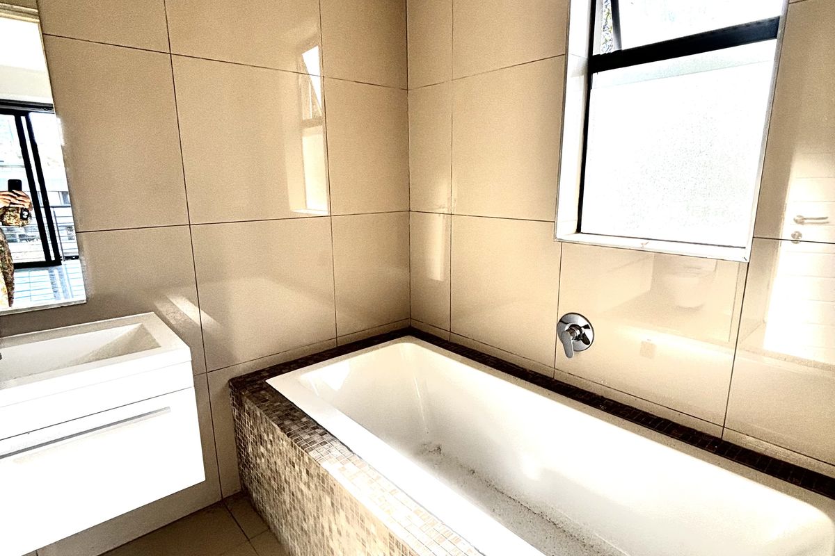 Modern bathroom featuring a built-in bathtub with mosaic tile surround, wall-mounted faucet, and a floating vanity unit with integrated basin.