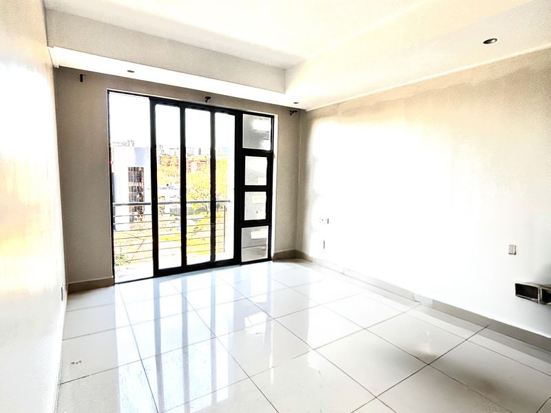 A bright, empty living room featuring large glass sliding doors leading to a balcony, polished floor tiles, and a wall-mounted air conditioning unit.