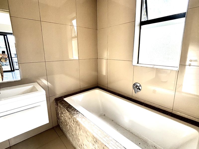 Modern bathroom featuring a built-in bathtub with mosaic tile surround, wall-mounted faucet, and a floating vanity unit with integrated basin.