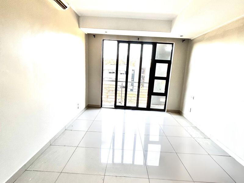 A bright, empty living area featuring large format floor tiles, a wall-mounted air conditioning unit, and sliding glass doors leading to an outdoor space.
