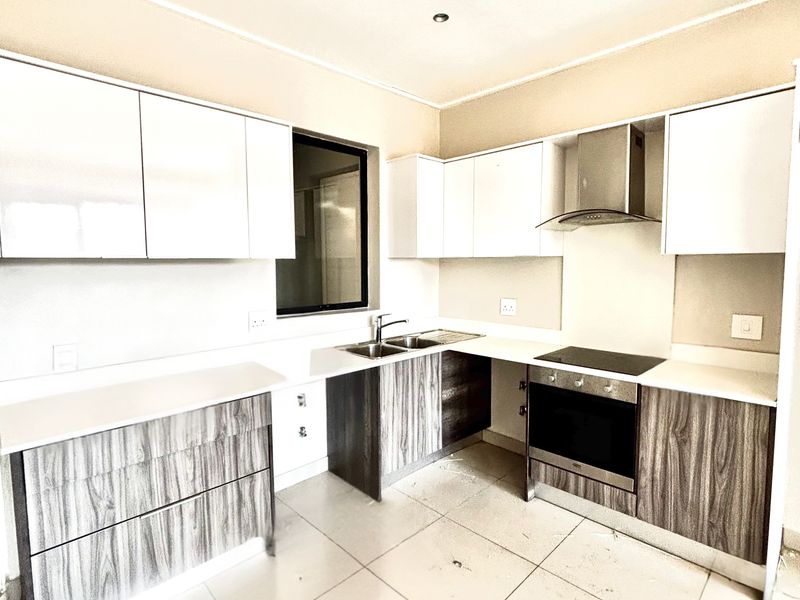Modern kitchen featuring two-tone cabinetry, integrated stainless steel oven, electric hob, extractor fan, and double sink with tiled flooring.